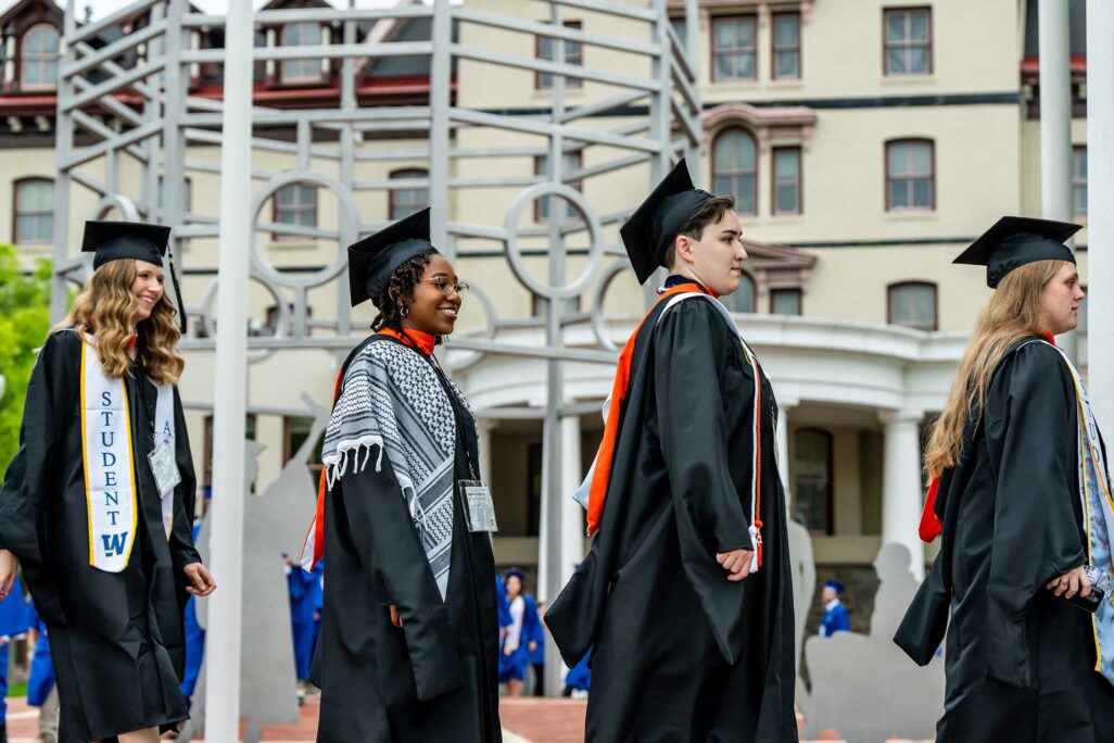 Widener University graduates walking in front of building in cap and gown